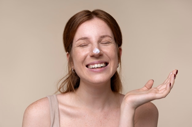 Portrait d'une jeune femme appliquant une crème hydratante sur son nez