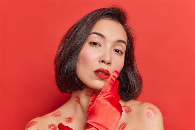 Portrait d'une jeune femme asiatique douce avec une peau saine et propre regarde tendrement la caméra a des poses naturelles de cheveux noirs pour la couverture du magazine semble séduisante isolée sur un mur de studio rouge vif