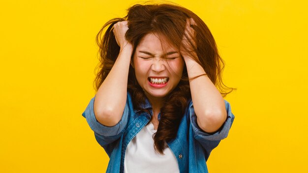 Portrait de jeune femme asiatique avec une expression négative, excité crier, pleurer en colère émotionnelle dans des vêtements décontractés et en regardant la caméra sur le mur jaune. Concept d'expression faciale.