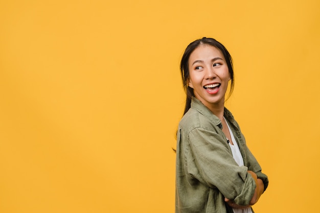 Portrait d'une jeune femme asiatique à l'expression positive, bras croisés, sourire largement, vêtue d'un tissu décontracté sur un mur jaune. Heureuse adorable femme heureuse se réjouit du succès. Concept d'expression faciale.