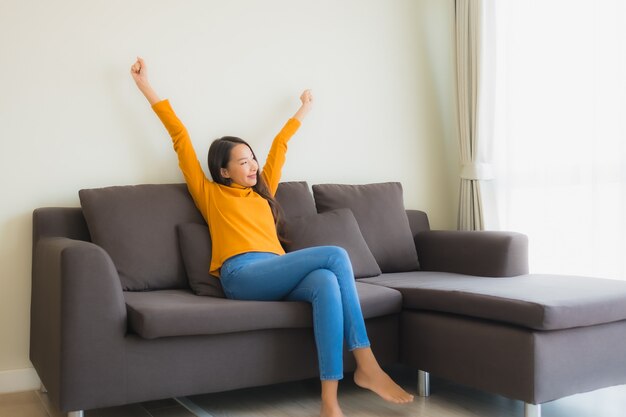 Portrait jeune femme asiatique heureuse se détendre sourire sur une chaise de canapé avec oreiller dans le salon