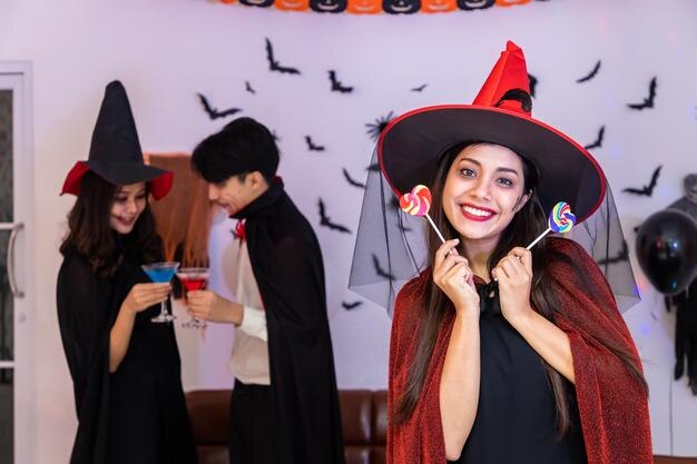 Portrait d'une jeune femme asiatique souriante en costume d'Halloween en tant que sorcière en fête tenant des bonbons en regardant la caméra