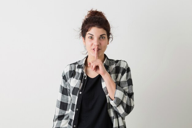 Portrait de jeune femme assez hipster tenant le doigt sur ses lèvres, émotion drôle, montrant le geste de silence, heureux, positif, isolé, chemise à carreaux