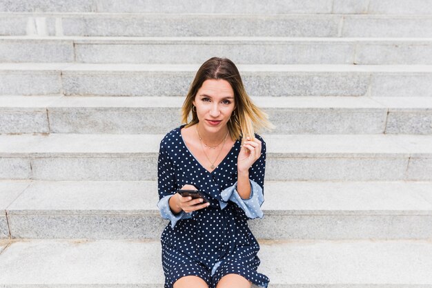 Portrait d&#39;une jeune femme assise sur l&#39;escalier avec téléphone portable