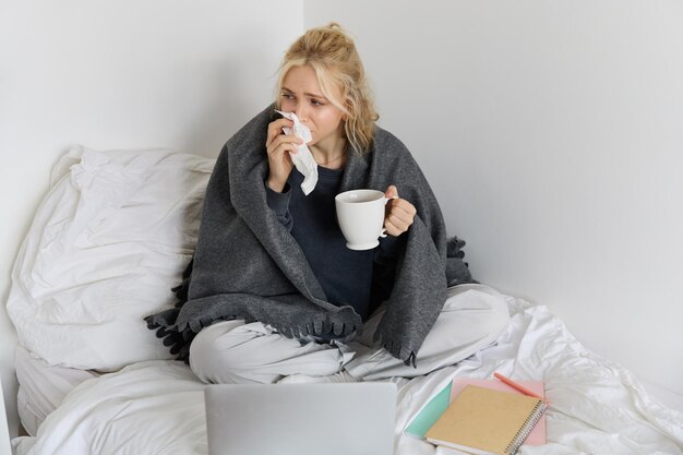 Portrait d'une jeune femme assise à la maison malade se sentant mal à l'aise buvant du thé passant du temps au lit a