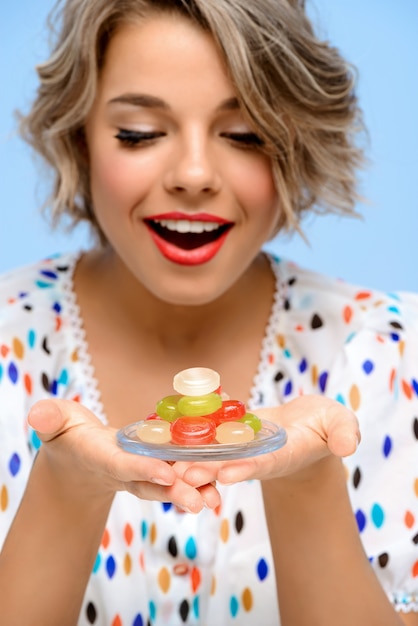 Photo gratuite portrait de jeune femme belle avec des bonbons sur le mur bleu