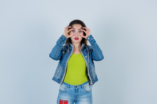 Portrait de jeune femme belle furtivement à travers les doigts en tenue de denim et à la vue de face focalisée