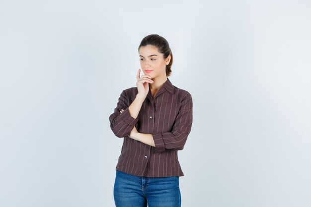 Portrait de jeune femme belle avec la main près du visage, regardant loin en veste et regardant la vue de face pensive