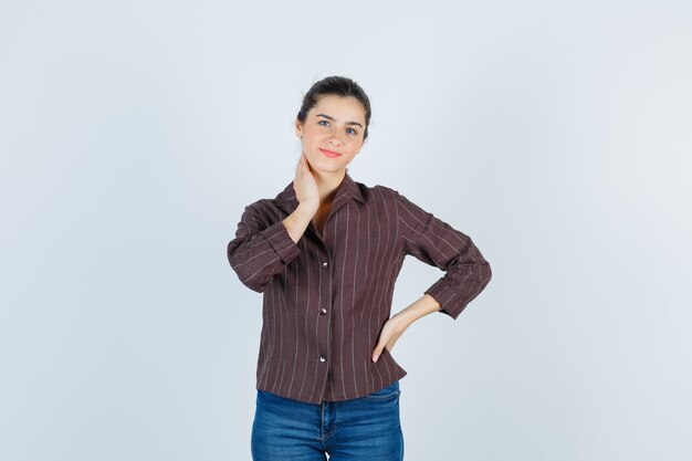 Portrait de jeune femme belle posant avec la main sur le cou dans la veste et à la vue de face heureuse