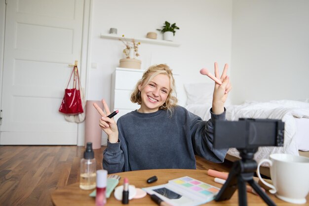 Portrait d'une jeune femme blonde, une adolescente qui enregistre une vidéo pour son compte de médias sociaux, montre du maquillage.