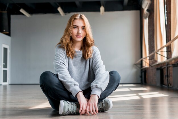 Portrait d&#39;une jeune femme blonde assise sur le sol en studio