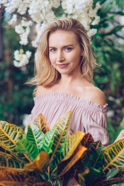 Portrait d&#39;une jeune femme blonde aux yeux gris, debout devant les feuilles