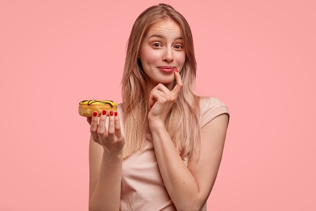 Portrait de jeune femme blonde avec beignet à la main