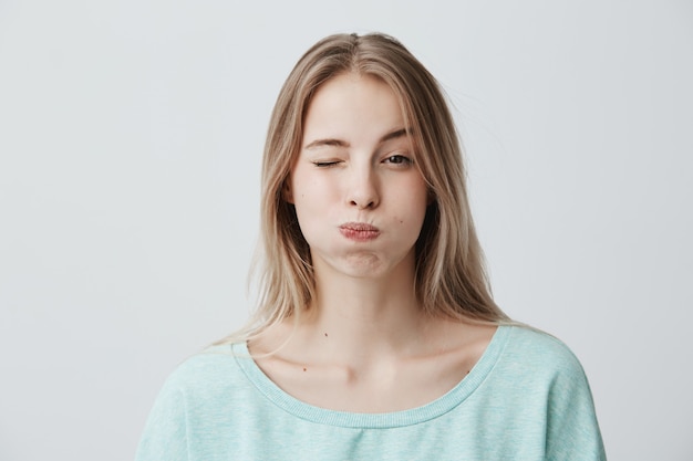 Portrait de jeune femme blonde fronçant les sourcils faisant la moue, clignotant