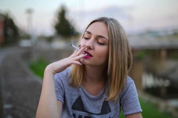 Portrait d'une jeune femme blonde fumeurs assis sur la route
