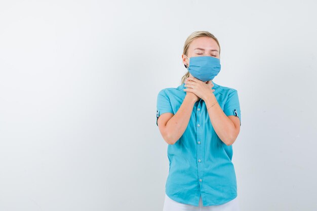 Portrait de jeune femme blonde gardant les mains sur le cou dans des vêtements décontractés isolés