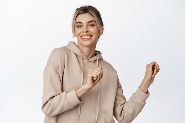 Portrait de jeune femme blonde avec un sourire blanc, dansant et ayant l'air heureux, posant sur blanc