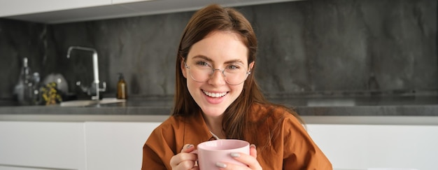 Portrait d'une jeune femme brune dans la cuisine se reposant à l'intérieur souriant et buvant du café savoureux