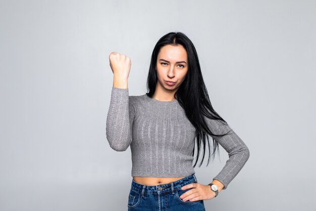 Portrait de jeune femme brune dominante montrant le poing sur le mur gris