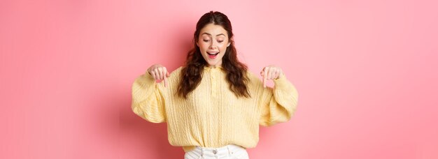 Portrait d'une jeune femme brune heureuse vérifiant l'offre promotionnelle pointant et regardant vers le bas avec étonnement