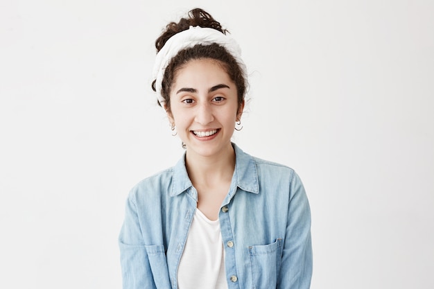 Portrait de jeune femme brune portant un chiffon et une chemise en jean étant de bonne humeur après avoir passé des week-ends avec des amis ou un petit ami, a des impressions positives.