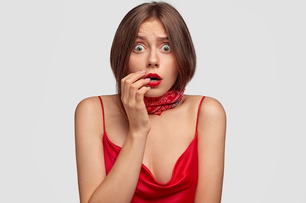 Portrait de jeune femme brune stupéfaite posant contre le mur blanc