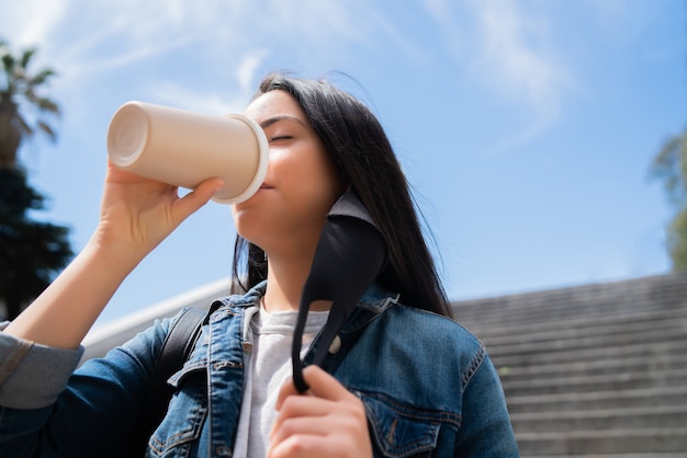 Portrait de jeune femme buvant une tasse de café en se tenant debout à l'extérieur dans la rue