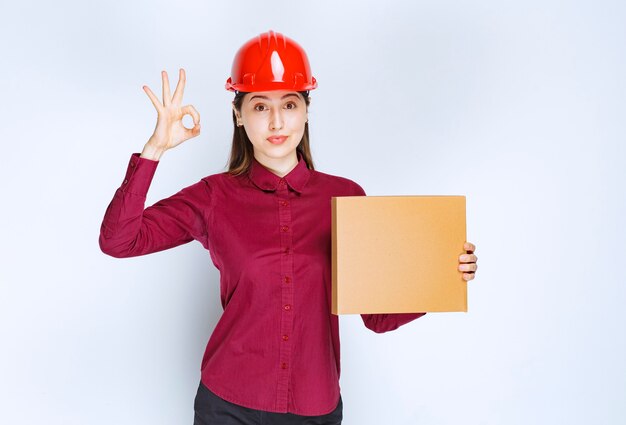 Portrait d'une jeune femme en casque de protection avec une petite boîte en papier montrant un geste correct.