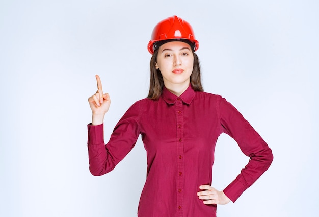 Portrait de jeune femme en casque de protection pointant vers le haut.