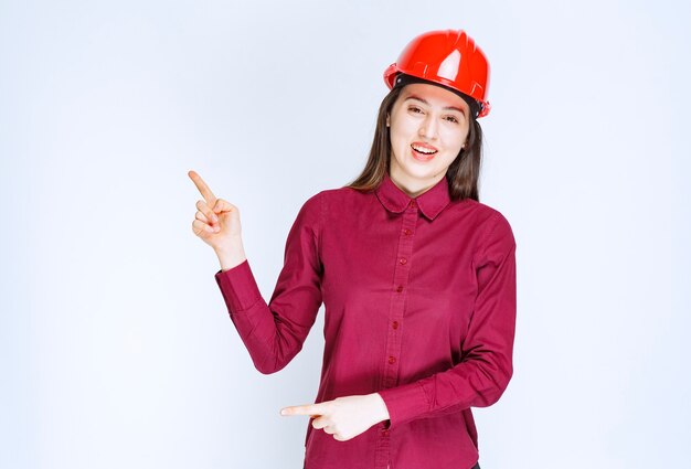 Portrait de jeune femme en casque de protection pointant vers le haut.