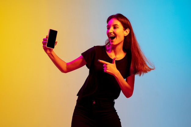 Portrait de jeune femme caucasienne sur fond de studio dégradé bleu-jaune en néon. Concept de jeunesse, émotions humaines, expression faciale, ventes, publicité. Beau modèle brune.