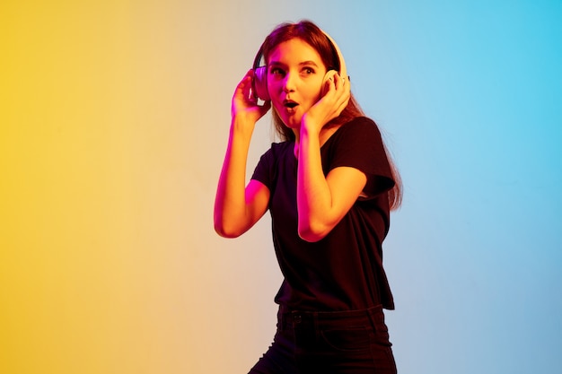 Portrait de jeune femme caucasienne sur fond de studio dégradé bleu-jaune en néon. Concept de jeunesse, émotions humaines, expression faciale, ventes, publicité. Beau modèle brune.