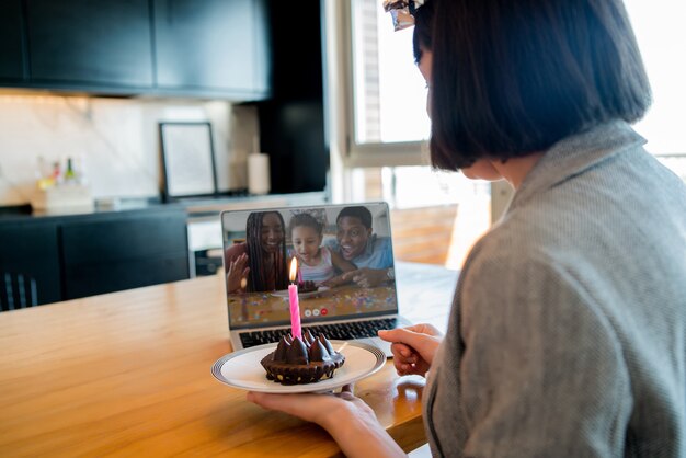 Portrait de jeune femme célébrant son anniversaire sur un appel vidéo avec ordinateur portable et gâteau à la maison