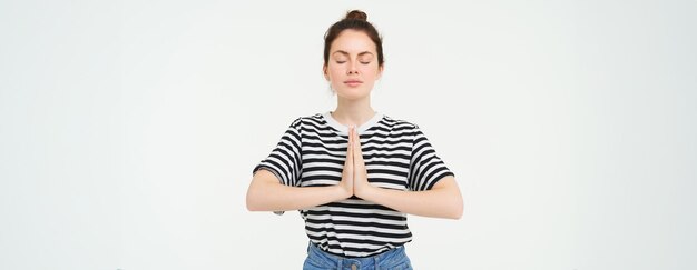 Portrait d'une jeune femme consciente en train de méditer, tenant les mains jointes ensemble, pratiquant le geste namaste