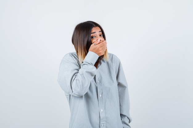 Portrait de jeune femme couvrant la bouche avec la main dans une chemise surdimensionnée et à la vue de face effrayée