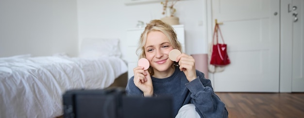 Photo gratuite portrait d'une jeune femme créatrice de contenu de beauté assise dans une pièce devant une caméra numérique