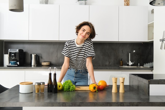 Photo gratuite portrait d'une jeune femme cuisinant de la salade une jolie fille végétalienne coupant des légumes sur le comptoir de la cuisine