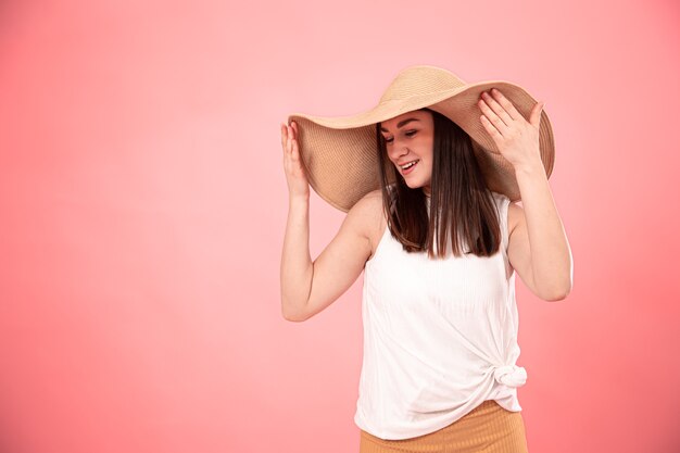 Portrait d'une jeune femme dans un grand chapeau d'été et un t-shirt blanc, sur fond rose. Le concept du look d'été.