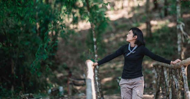 Portrait jeune femme debout sur un pont en bambou sourire et à la belle nature tout en camping en forêt avec espace de copie heureux