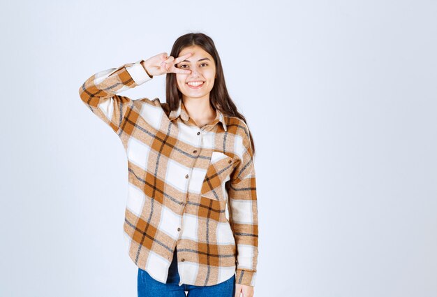 Portrait de jeune femme debout et souriant à la caméra sur un mur blanc.