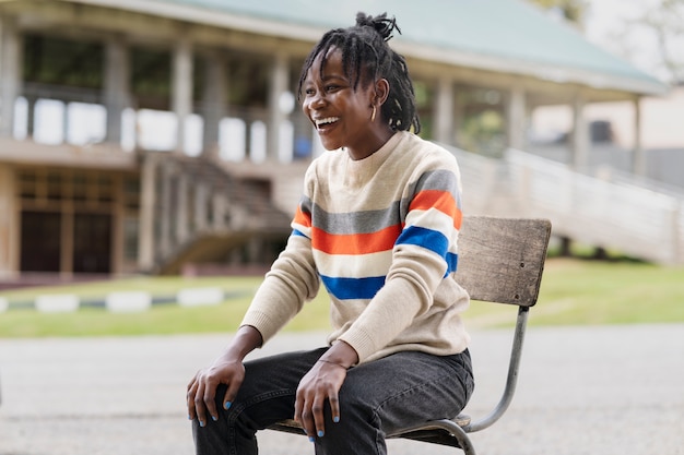 Portrait de jeune femme avec des dreadlocks afro assis sur une chaise à l'extérieur