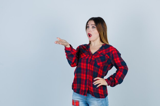 Portrait de jeune femme écartant la paume tout en regardant loin en chemise à carreaux et à la vue de face choquée