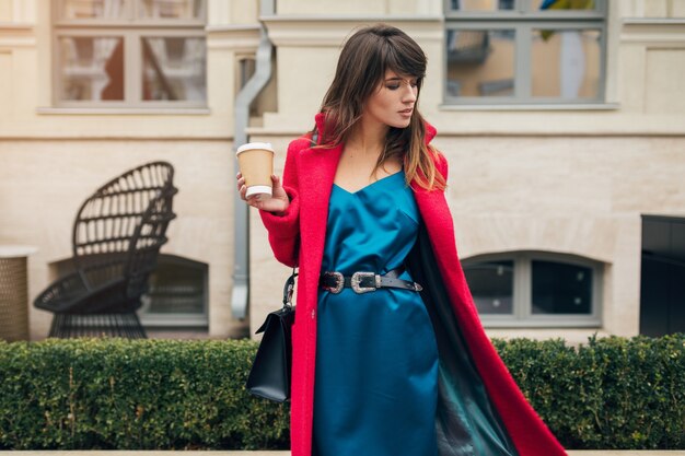 Portrait de jeune femme élégante belle souriante marchant dans la rue de la ville en manteau rouge, boire du café