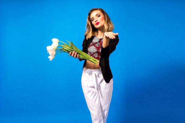 Portrait de jeune femme élégante avec maquillage lumineux et blazer sombre, tenant des fleurs blanches