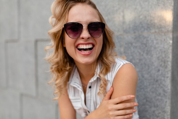 Portrait de jeune femme élégante et séduisante souriant marchant dans la rue de la ville en robe de style mode d'été portant des lunettes de soleil sourire candide