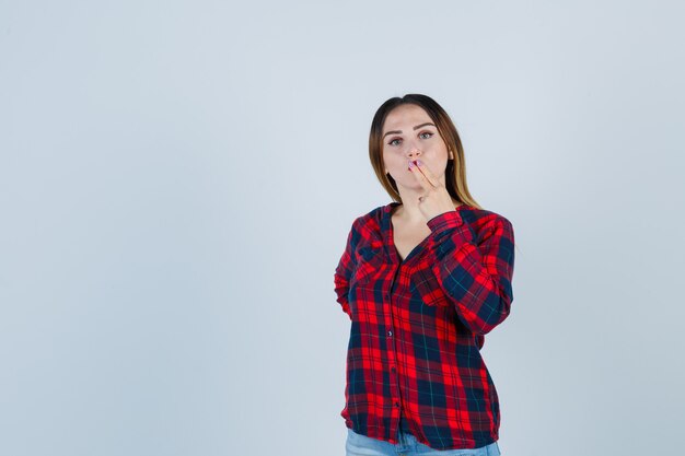 Portrait de jeune femme embrassant ses doigts en chemise à carreaux et à la vue de face confiant