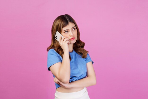 Portrait d'une jeune femme ennuyée portant un t-shirt décontracté parlant sur un téléphone portable isolé sur fond rose