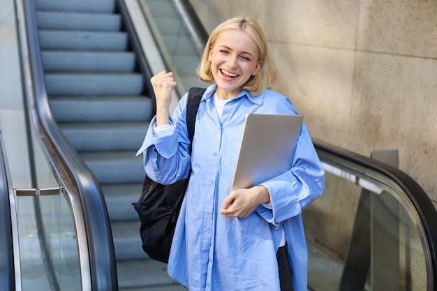 Photo gratuite portrait d'une jeune femme enthousiaste qui célèbre ou triomphe en tenant un ordinateur portable et