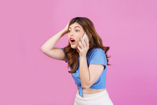 Portrait d'une jeune femme excitée portant un t-shirt décontracté parlant sur un téléphone portable isolé sur fond rose