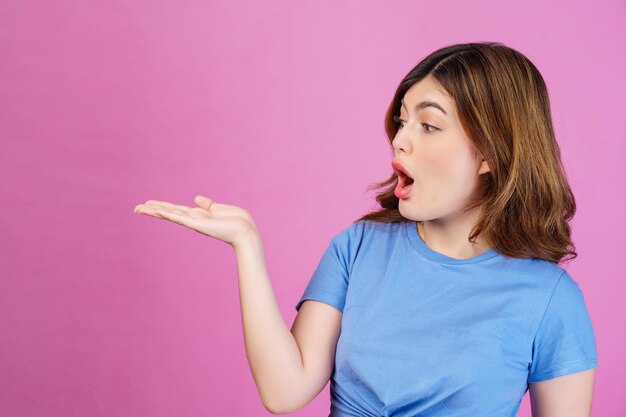 Portrait d'une jeune femme excitée portant un t-shirt décontracté tenir la main démontrer l'offre d'annonces promotionnelles isolées sur fond rose